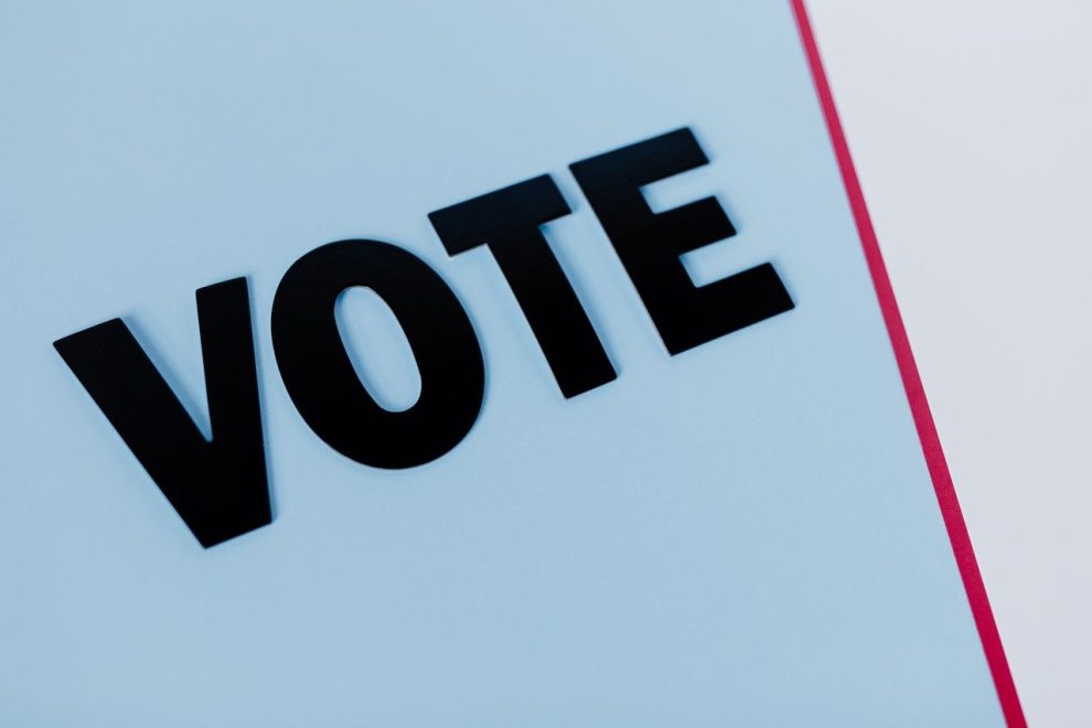 Close-up da palavra “VOTE” em composição minimalista sobre fundo claro.