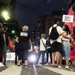 Grupo de pessoas participa de um protesto feminista à noite, em uma rua da cidade.
