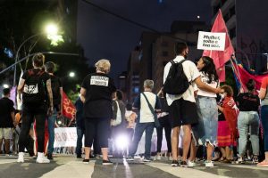 Grupo de pessoas participa de um protesto feminista à noite, em uma rua da cidade.