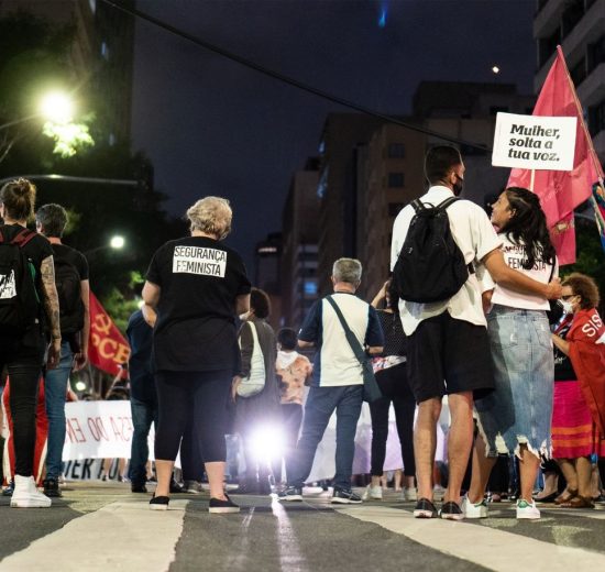 Grupo de pessoas participa de um protesto feminista à noite, em uma rua da cidade.