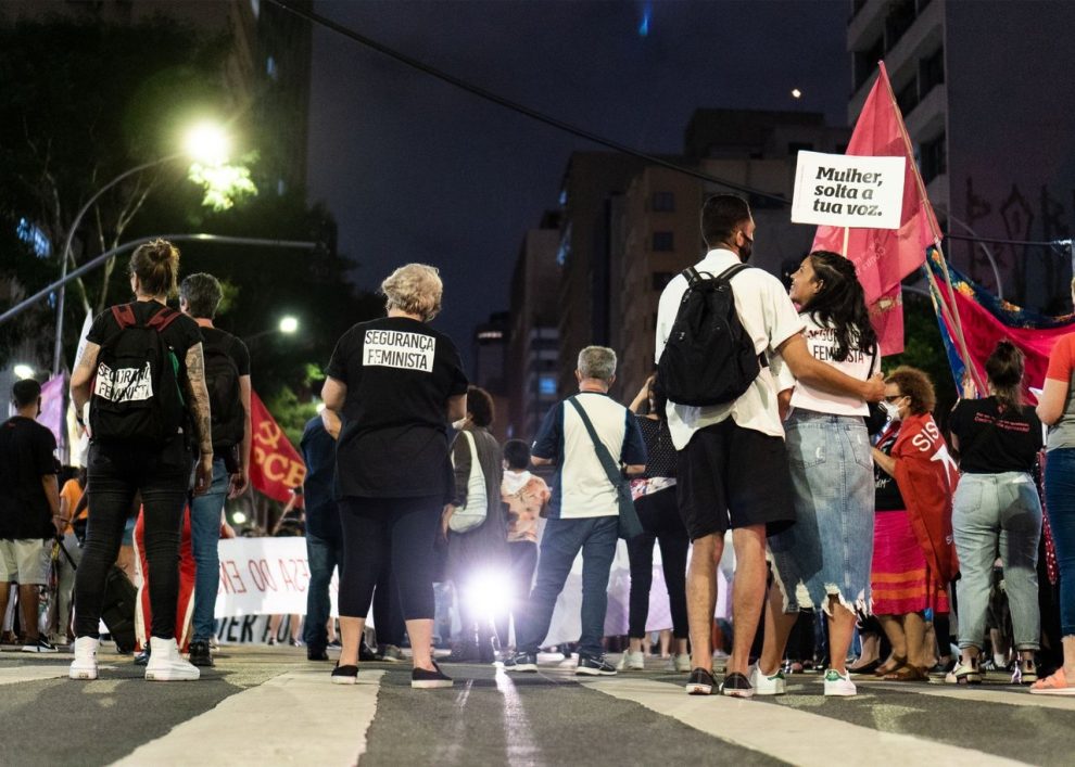 Grupo de pessoas participa de um protesto feminista à noite, em uma rua da cidade.